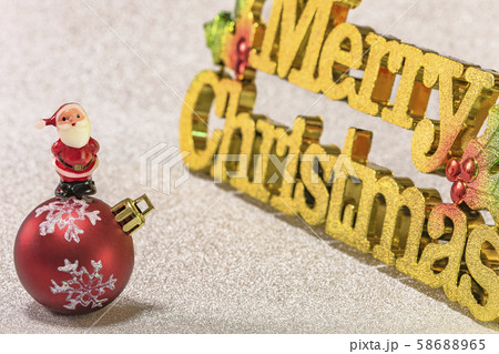 ラメの金紙黄金の文字で書いてあるメリークリスマスとクリスマスツリーの飾りボールとサンタクロースの人形 58688965