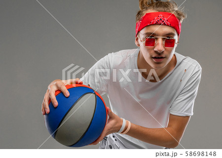 cool young man on a gray background with a ball in his hands, half shot of a teenager in a light T 58698148