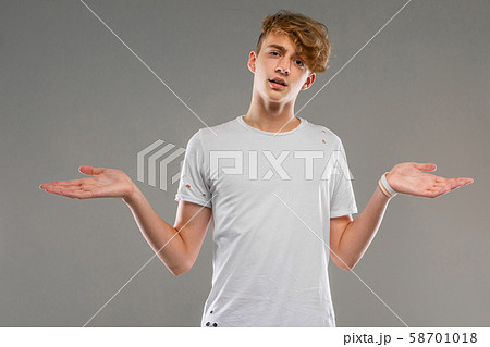handsome emotional teenager boy posing in studio against gray, young man in a light T-shirt spreads 58701018