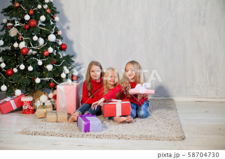 Three girl sisters open Christmas gifts at the Christmas tree new year Three girl sisters open Christmas gifts at the Christmas tree new year 58704730