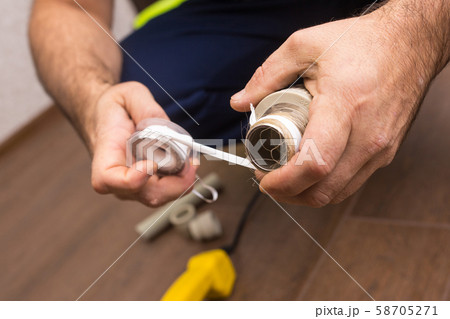 Preparing to connect the water supply. Winding the tape. Hands plumbing close-up. Preparing to connect the water supply. Winding the tape. Hands plumbing close-up. 58705271