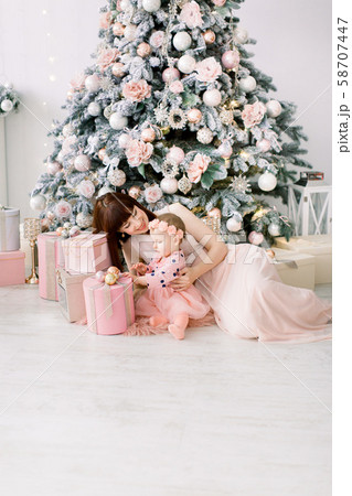 A beautiful mother with a small daughter in pink dresses playing around a decorated Christmas tree 58707447
