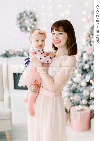Happy family woman mother and little girl relax playing near Christmas tree on Christmas eve at home 58707575
