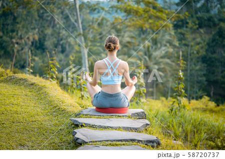 Young woman on path into the tropical jungle in yoga lotus pose Young woman on path into the tropical jungle in yoga lotus pose 58720737