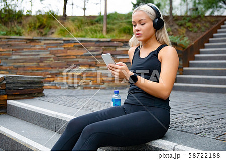 Beautiful sports woman sitting at stairs listen to music from smartphone Beautiful sports woman sitting at stairs listen to music from smartphone 58722188