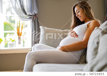 Smiling pregnant woman sitting in sofa looking at her stomach 58723955