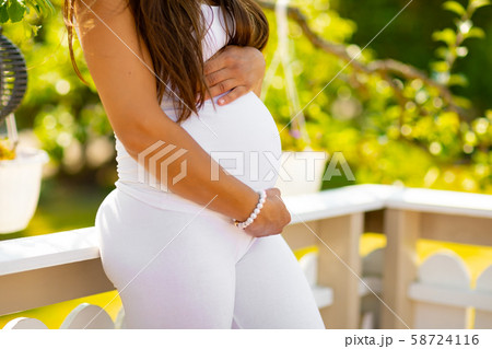 Close-up of pregnant woman standing in garden holding hands on belly 58724116