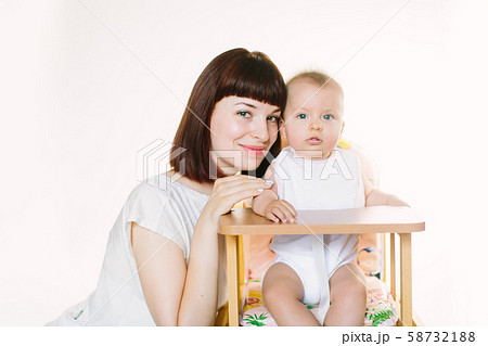 Young beautiful mother puts a white bib on her baby girl, sitting at a chair. 58732188