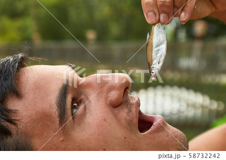 Holding a very small fish above open mouth Holding a very small fish above open mouth 58732242