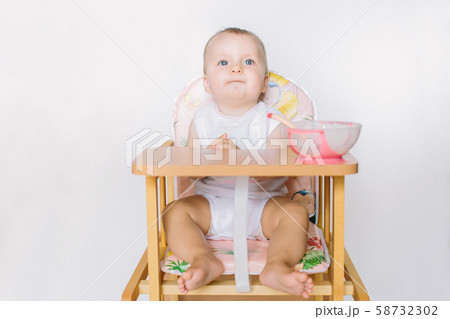 The baby is sitting on the chair and is preparing for feeding. 58732302