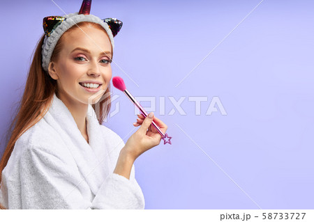 Beauty Portrait of beautiful woman applying cosmetic with brush isolated on purple background 58733727