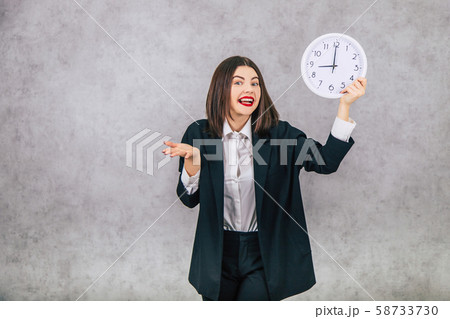 Pretty female employee raising up the white clock, smiling, happily, holding her hand as if she 58733730