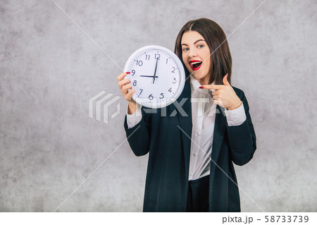 Pretty office female employee standing, pointing her finger at the clock in her hand. 58733739