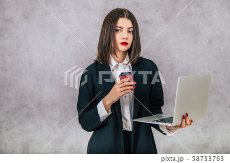Serious cute businesslady holding a latop and a cup of coffee, looking at the camera. 58733763
