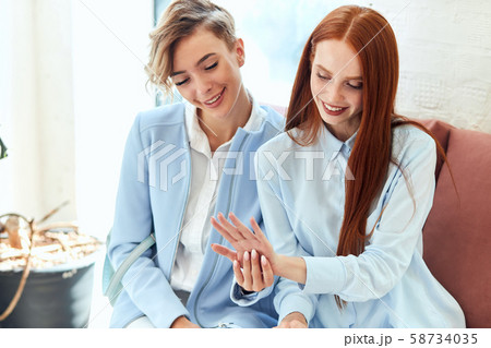Two positive young caucasian women sit on sofa and show manicure Two positive young caucasian women sit on sofa and show manicure 58734035