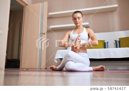 Portrait of attractive young sporty woman wearing white clothing doing yoga exercise in room Portrait of attractive young sporty woman wearing white clothing doing yoga exercise in room 58741427
