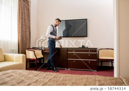 Young elegant hotel porter with touchpad touching piece of wooden furniture 58744314
