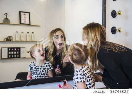 Mother and daughter applying lipstick in mirror Mother and daughter applying lipstick in mirror 58748327