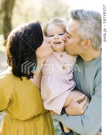 Parents kissing their daughter's cheeks 58748357