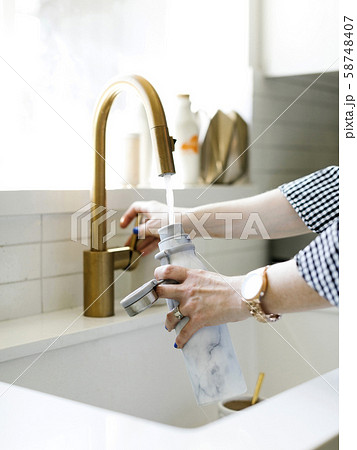 Hands of woman filling water bottle in kitchen sink Hands of woman filling water bottle in kitchen sink 58748407