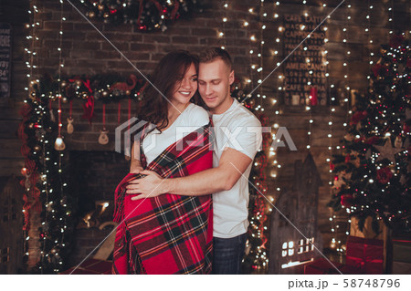 Lovely couple woman and man are covered in blanket at home near fireplace. Christmas time. 58748796