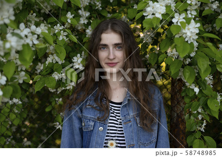 Young woman wearing denim jacket by white flowers Young woman wearing denim jacket by white flowers 58748985