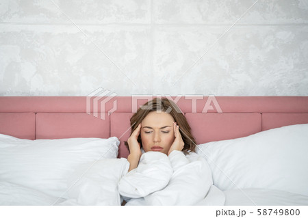 Low-spirited young woman with headache lying in bed 58749800