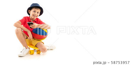 A little boy in panama, yellow jersey, red shorts and white sneakers sits on a yellow penny and 58753957