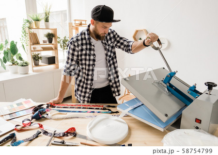 Young creative man printing or sticking decor on one of pet collar workpieces Young creative man printing or sticking decor on one of pet collar workpieces 58754799