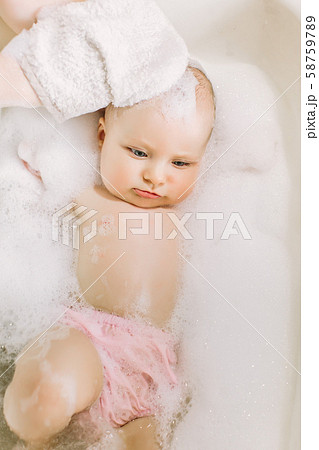 Happy laughing baby taking a bath playing with foam bubbles. Little child in a bathtub. Infant 58759789