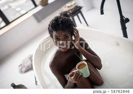 Dark-eyed woman drinking morning coffee while having bath Dark-eyed woman drinking morning coffee while having bath 58762846