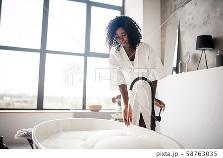 Curly dark-skinned woman preparing bath with foam 58763035