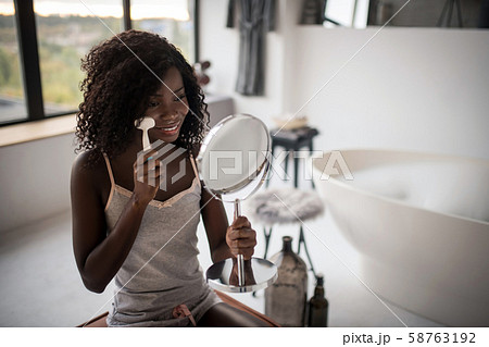 Curly woman looking into mirror while cleaning her skin Curly woman looking into mirror while cleaning her skin 58763192