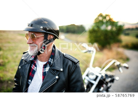 A cheerful senior man traveller with motorbike in countryside, walking. A cheerful senior man traveller with motorbike in countryside, walking. 58765769