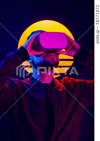 Man wearing virtual reality goggles. VR head set videogame in 80's synthwave and retrowave futuristic aesthetics. 58771872