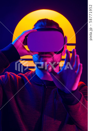 Man wearing virtual reality glasses headset. Vr world experience. Videogame in 80's synthwave and retrowave futuristic aesthetics. 58771952