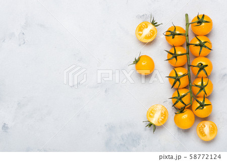 Yellow cherry tomatoes on branch, whole on cut in half, on rustic table top view with copy space. 58772124