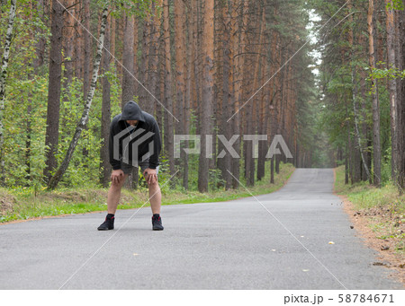 Tired man in grey hoodie making a stop after jogging on road in the forest, selective focus 58784671