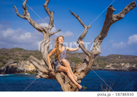 Woman sitting on a tree against the background of the sea Angel's Billabong in Nusa Penida, Bali 58786930