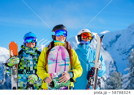 Happy man and woman with snowboard and skis standing on snow resort against backdrop of mountain in Happy man and woman with snowboard and skis standing on snow resort against backdrop of mountain in 58788324