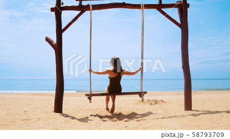 Young woman in swimsuit is riding on a swing on the beach 58793709