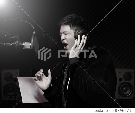 Asian Teenager man black hair earmuff headphone sing a song loudly power sound over hanging microphone condenser, speakers, composer note book and monitor. Studio Sound Proof Absorbing wall room 58796279