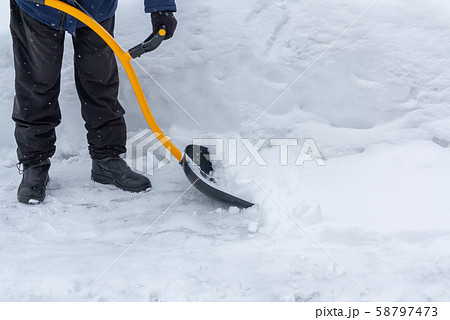 A man cleans snow in the yard with a shovel after a heavy snowfall A man cleans snow in the yard with a shovel after a heavy snowfall 58797473