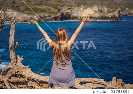 Woman sitting on a tree against the background of the sea Angel's Billabong in Nusa Penida, Bali 58798895