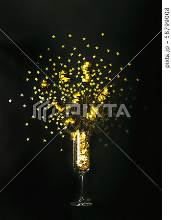 Golden star shaped confetti and party streamers poured out of champagne glass on black background Golden star shaped confetti and party streamers poured out of champagne glass on black background 58799008