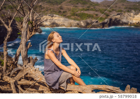 Woman sitting on a tree against the background of the sea Angel's Billabong in Nusa Penida, Bali 58799018
