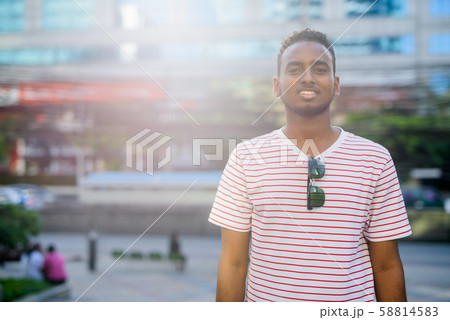 Happy young African bearded man with Afro hair smiling in the city 58814583