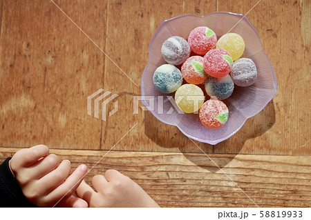 ガラス皿の上のカラフルな飴玉と小さな女の子の手 58819933
