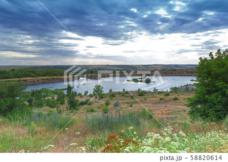Scenic view on flooded quarry with blue water under cloudy sky with green fields and trees around it Scenic view on flooded quarry with blue water under cloudy sky with green fields and trees around it 58820614