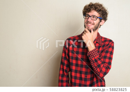 Happy young bearded hipster man with curly hair thinking 58823825